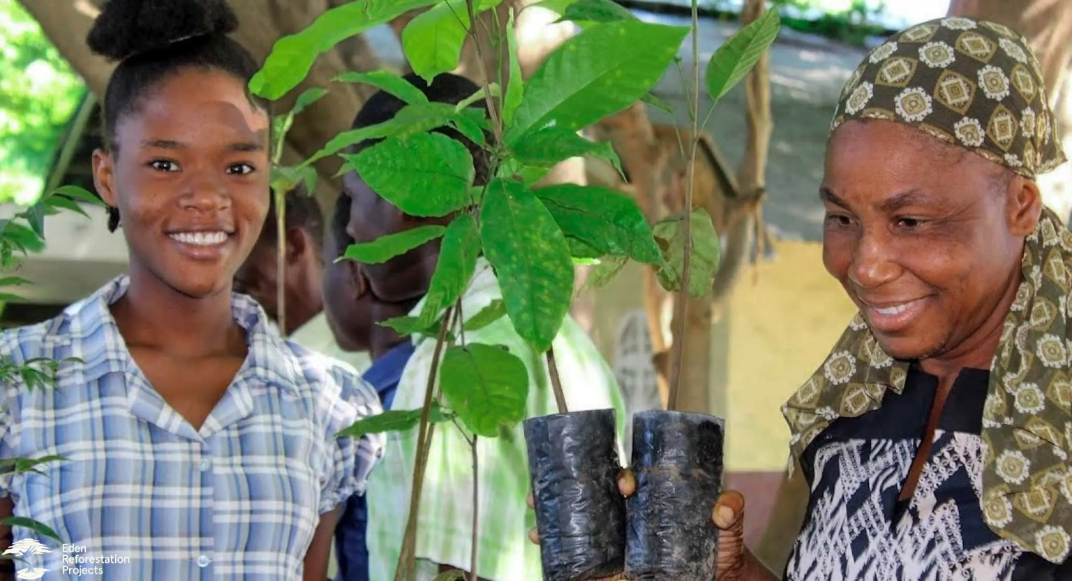 Two women smiling holding a young tree